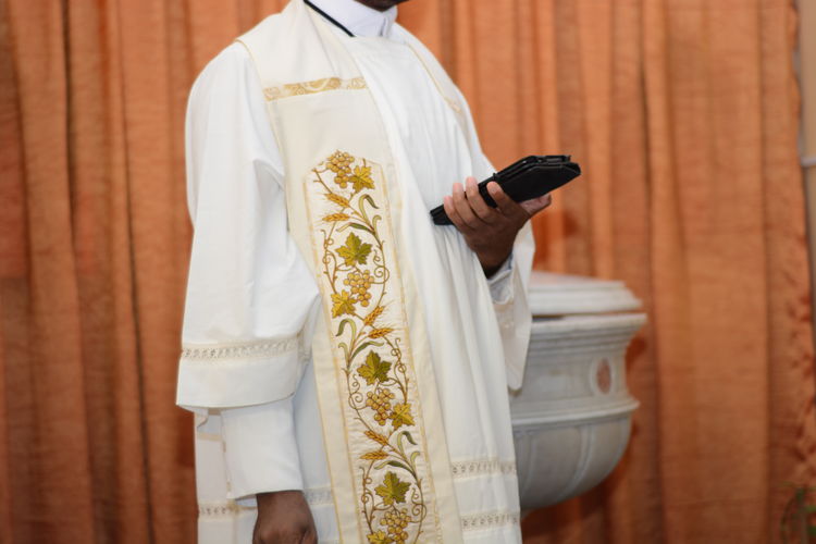 Midsection of priest holding bible while standing against curtain in church