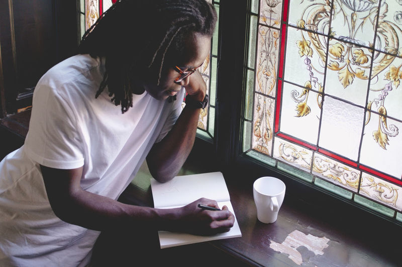 High angle view of businessman writing in book by window in creative office
