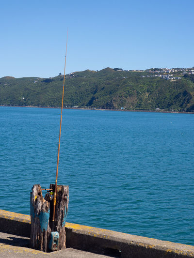 Fishing rod by sea against clear blue sky