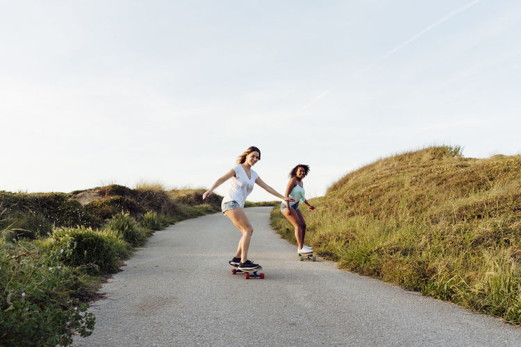 Beautiful multiethnic women skaters riding skate board down the road in countryside towards camera