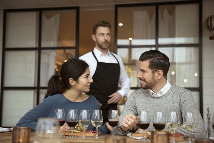 Business people discussing during wine tasting against man wearing apron looking away