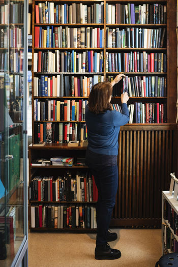 Rear view of librarian arranging books on shelf in store