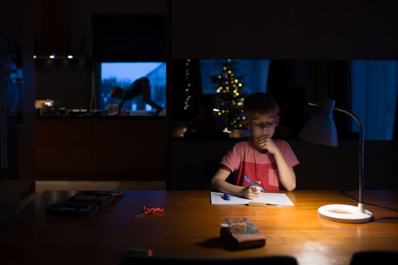 Boy sitting on table in illuminated room
