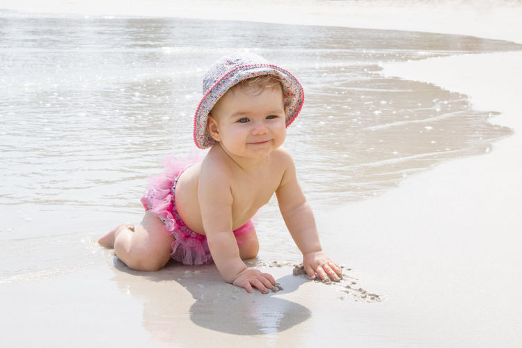 Smiling little girl is playing with sand at beach near to sea. sensory development for kids. 