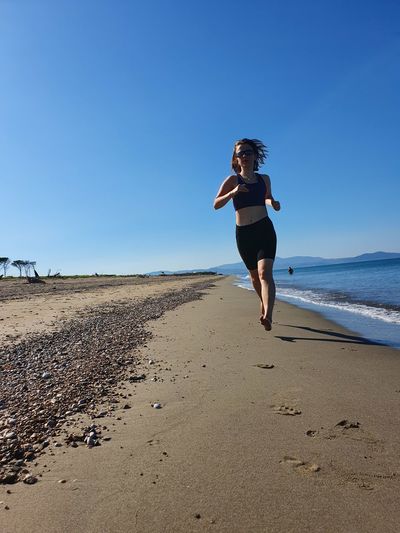 Woman running on beach against clear blue sky