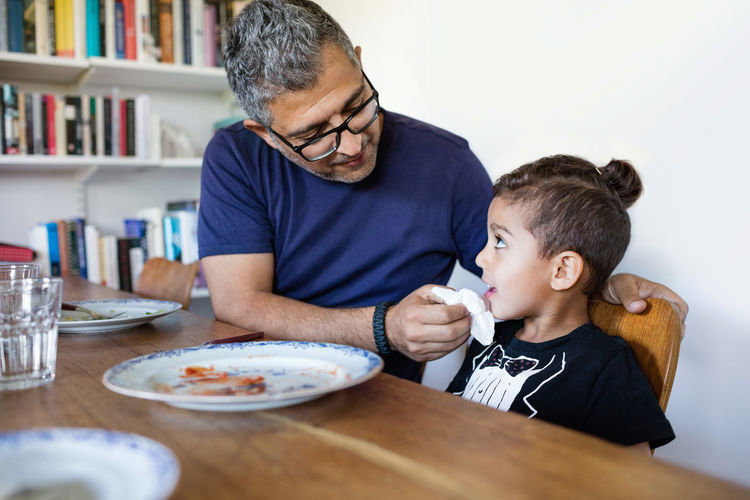 Father wiping son's mouth after lunch at dining table