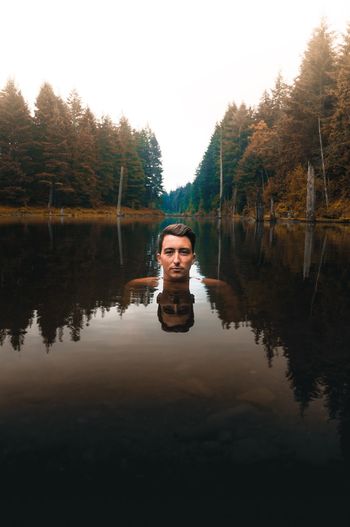 Portrait of young man swimming in lake against clear sky at forest