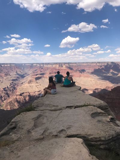 People sitting on cliff against sky