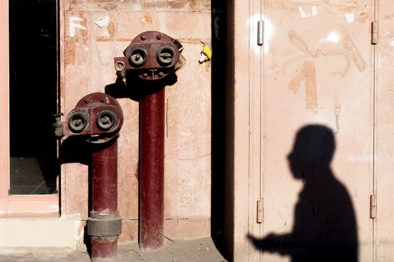 Shadow of man by fire hydrant against wall