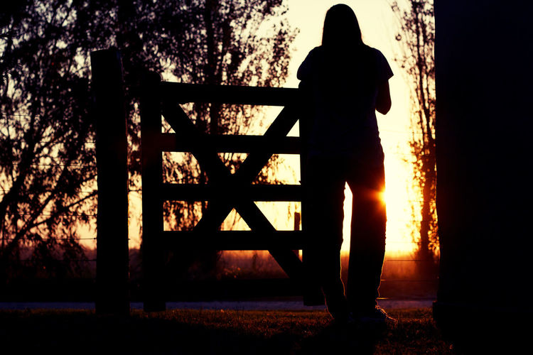 Silhouette woman standing by railing against sky during sunset