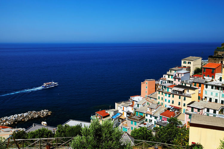 Buildings at manarola by passenger craft in sea against clear blue sky