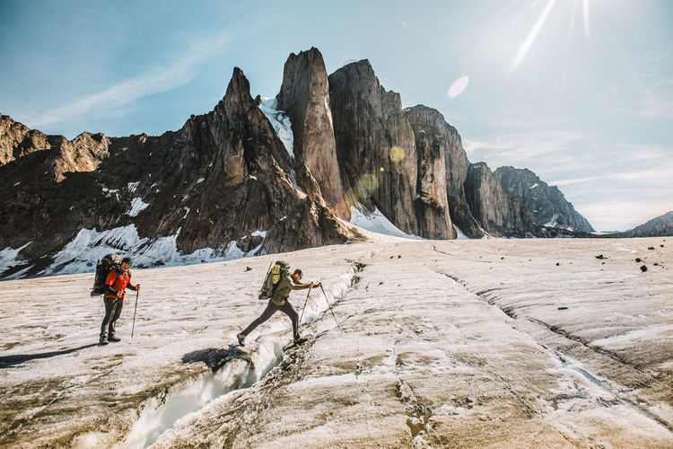 Mounatineer crosses a glacial crevasse on a sunny day, baffin island.