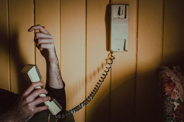 Cropped image of person holding telephone on wall