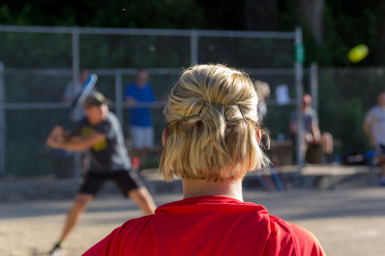 Rear view of girl looking at men playing baseball on playing field