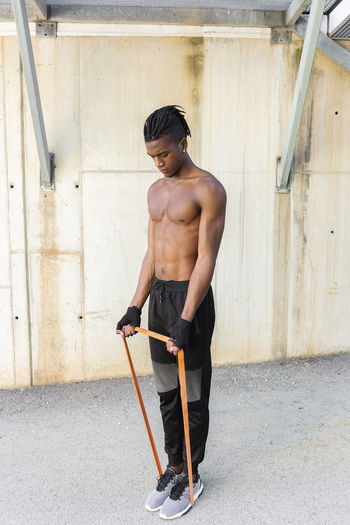 Shirtless young man exercising with resistance band outdoors