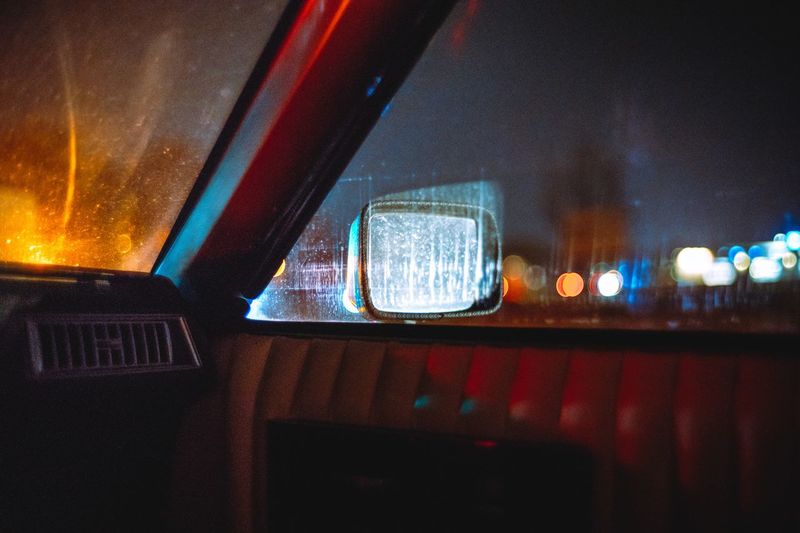 Car on illuminated street seen through wet window