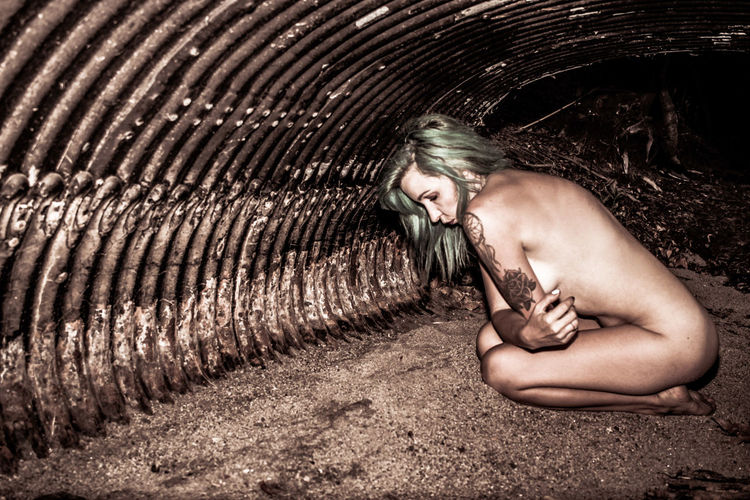 Side view of naked punk kneeling in cave at night