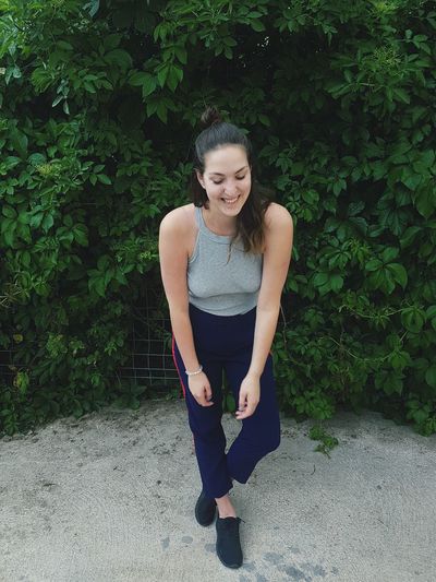 Full length of smiling young woman standing against plants