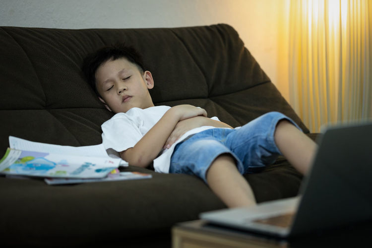 Boy sleeping on sofa with books at home