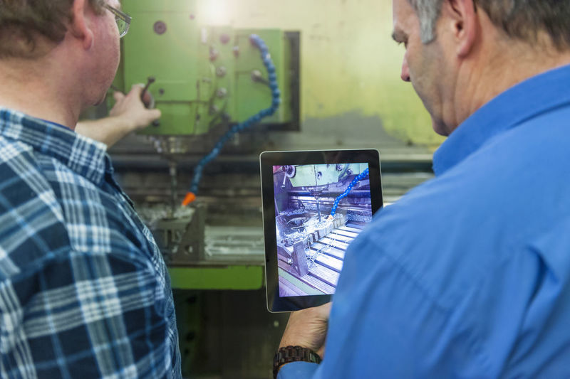 Two men in factory with digital tablet at a machine
