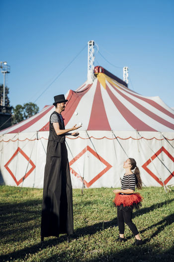 Male artist with stilts talking to female acrobat while standing on meadow