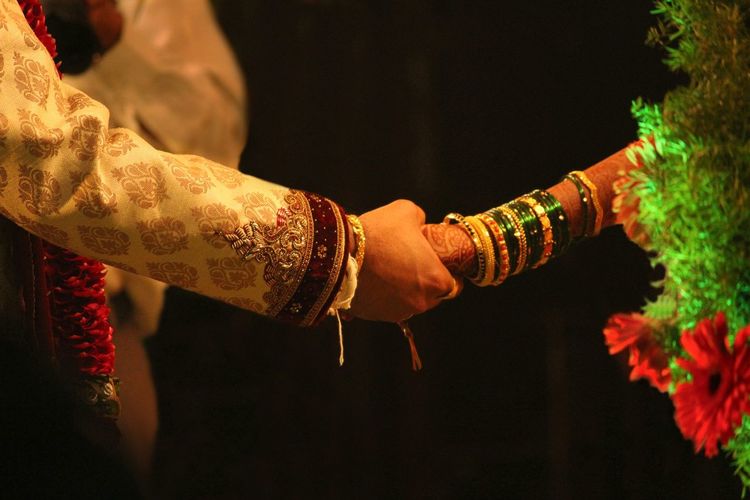 Midsection of couple holding hands against black background during wedding