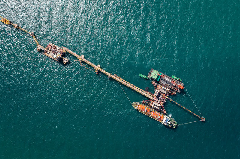 Aerial view oil pipes to oil tanker ships at pier off the coast in beautiful peaceful environment.