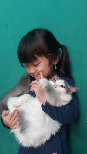 Cute girl carrying cat while standing against blue background