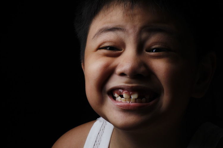 Close-up of boy clenching teeth against black background