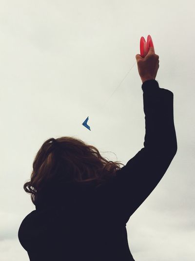 Rear view of woman flying kite against cloudy sky