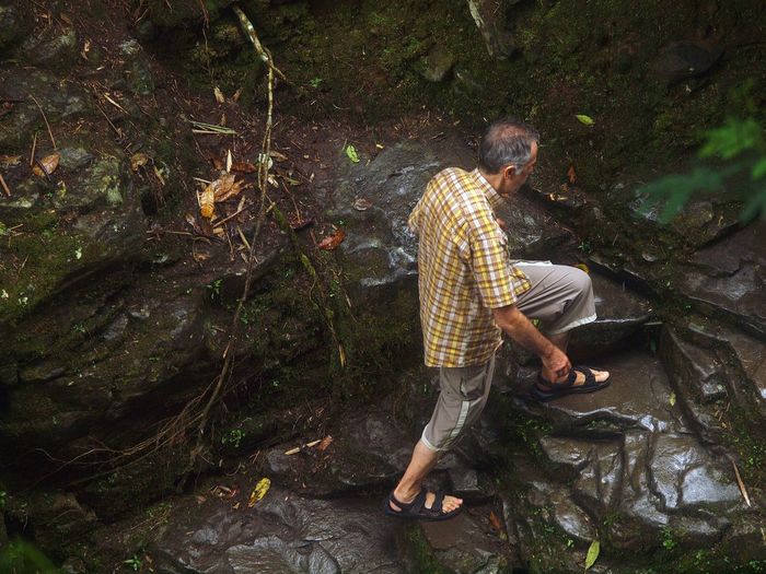 High angle view of man climbing wet rocks in forest
