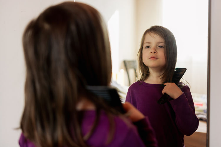Child combing her hair in front of a mirror
