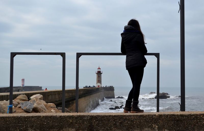 Rear view of woman standing by railing and sea against sky