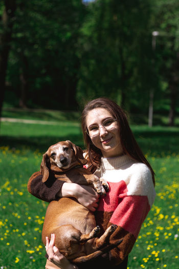 Charming young lady dressed in coloful sweater holding daschund dog and kissing. animal love concept