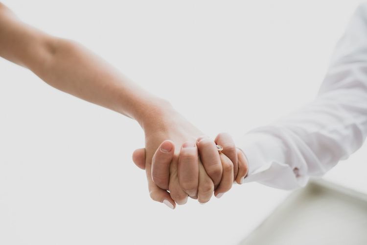 Cropped image of couple holding hands against white background