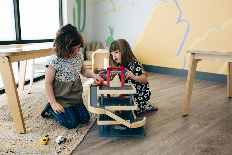 Two girls sit on the floor and play together with a car ramp toy