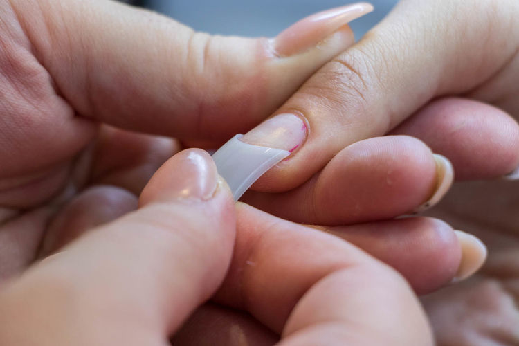 Close-up of hand attaching artificial nail on customer fingers
