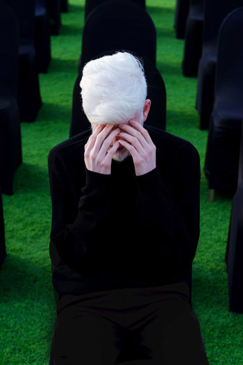 Portrait of an albino man with hands over his eyes sitting on the chair