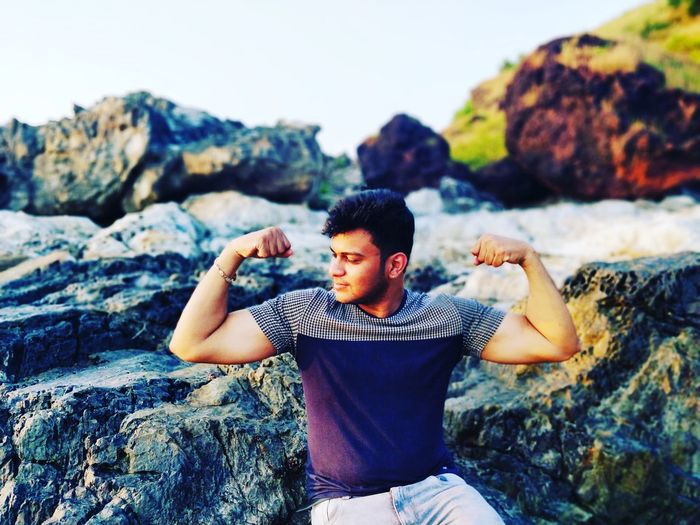 Young man flexing muscles while sitting on rock