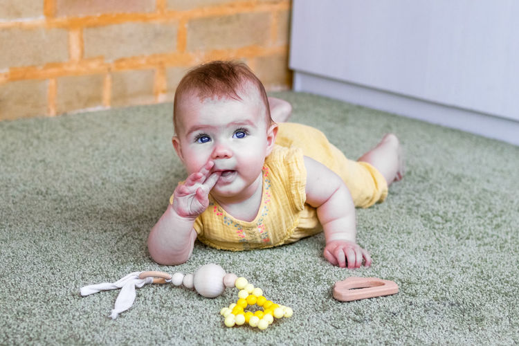 Little caucasian baby girl is playing with wooden and silicon teething toy.