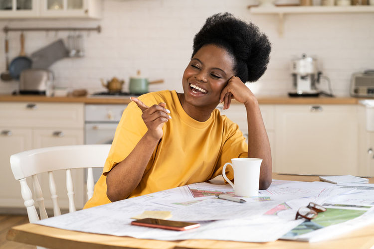 Overjoyed black businesswoman laugh work from home. cheerful architect sit at table with blueprints