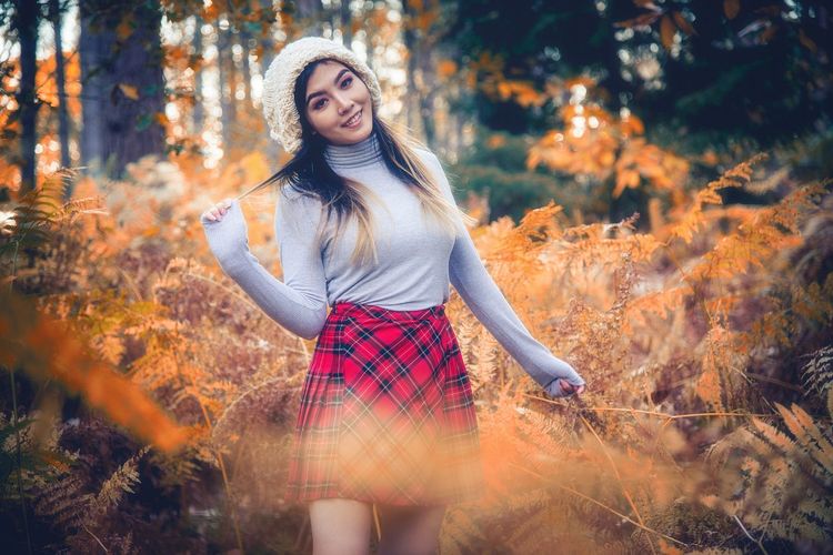 Portrait of smiling young woman standing in forest during autumn