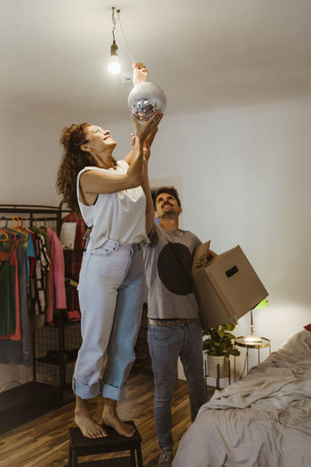 Man helping girlfriend installing disco ball by illuminated light bulb at home