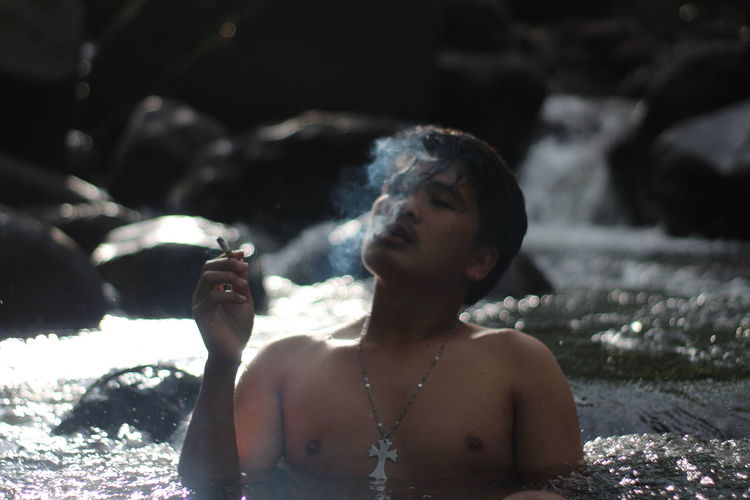 Young man smoking cigarette while relaxing in stream water