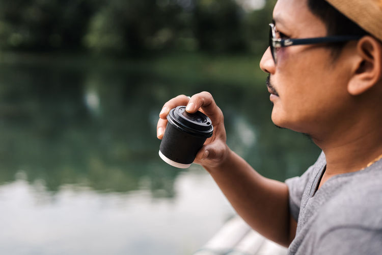 Cropped hand of person holding coffee cup by lake