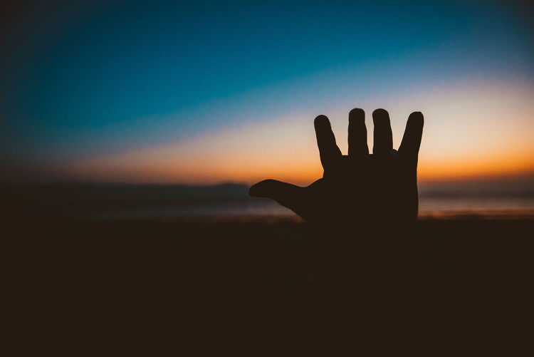 Close-up of silhouette hand against sky during sunset