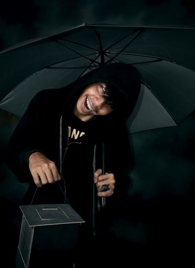 Portrait of smiling young man holding umbrella while standing against black background