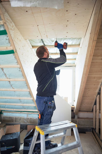Man drilling wooden planks on roof beam in house