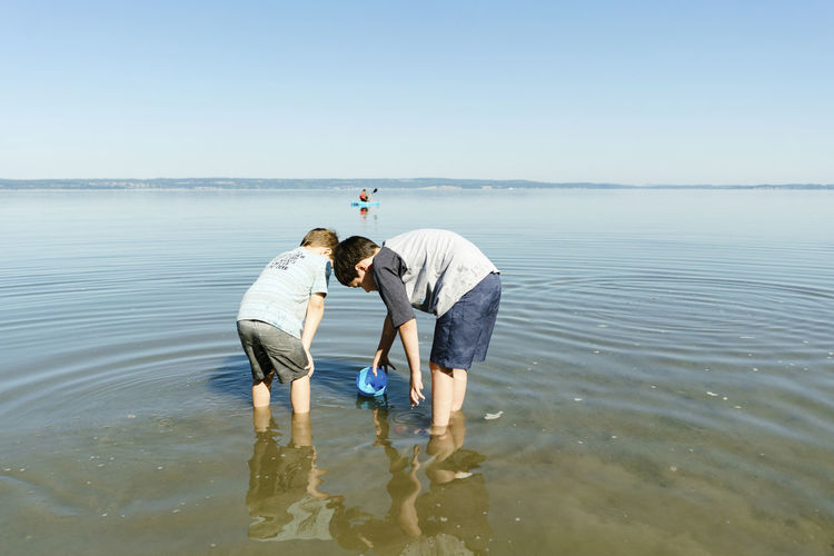 Brothers playing with water while standing in sea against clear blue sky during sunny day