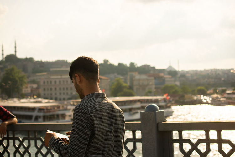 Rear view of man sitting on railing against river